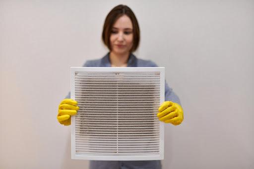 A woman wearing yellow gloves holding a dirty HVAC air filter.